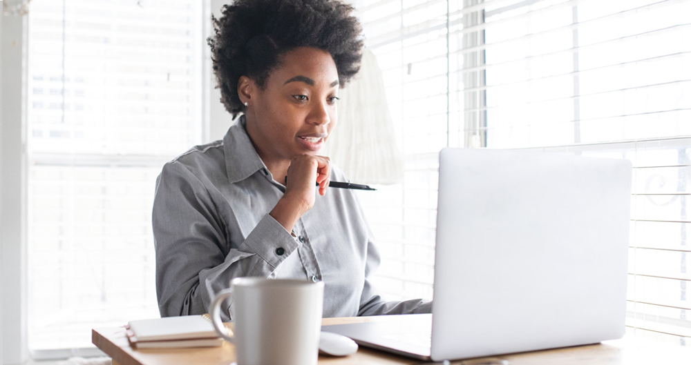 Une femme assise à un bureau faisant un appel avec un ordinateur portable.